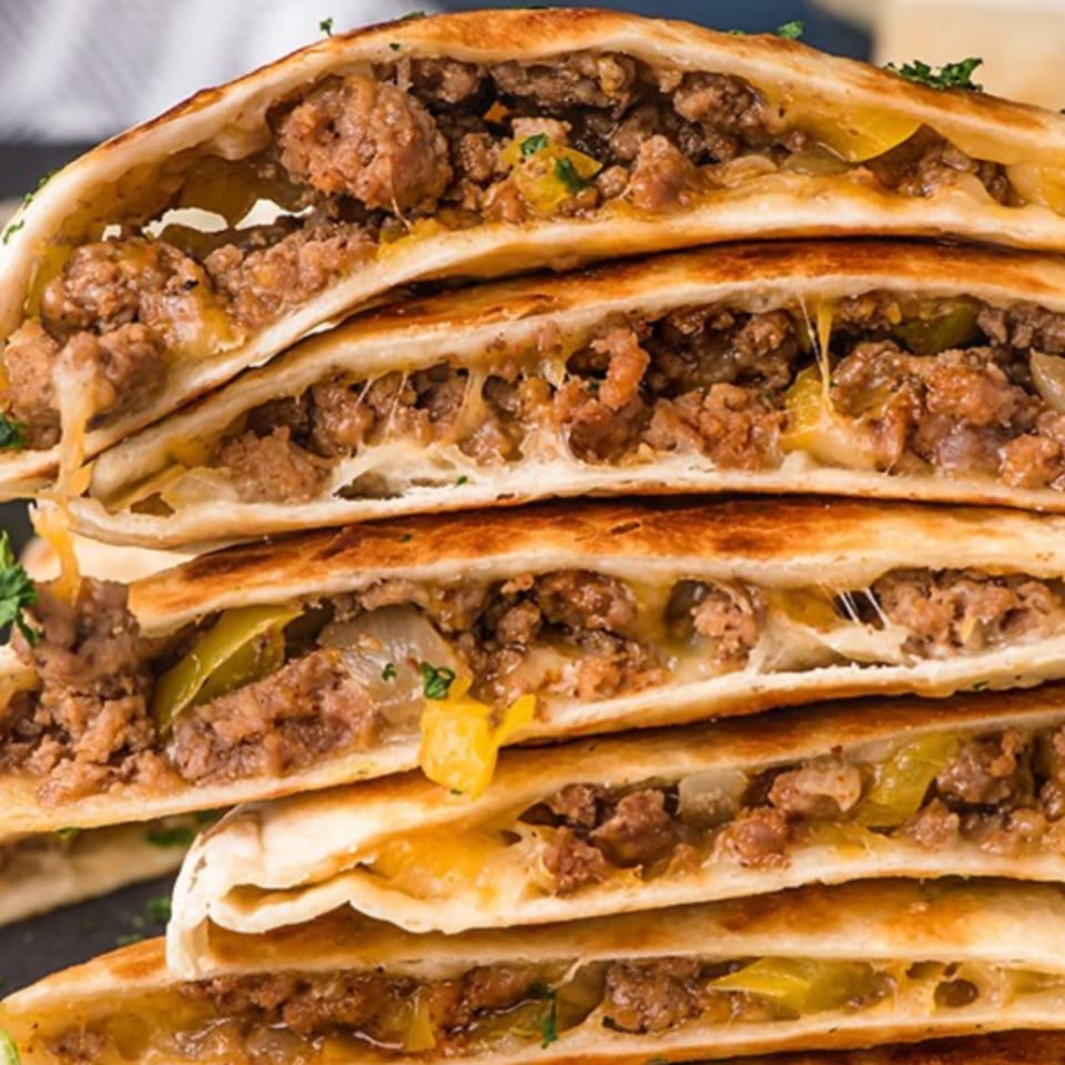 Stack of El Pollito Pio's Mexican quesadillas, filled with seasoned ground meat, melted cheese, and peppers.