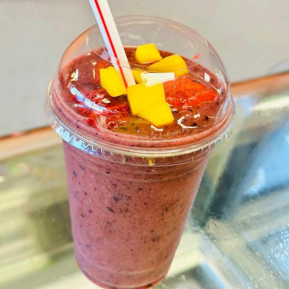 A vibrant El Pollito Pio berry smoothie with mango and strawberry chunks, and a red-striped straw.