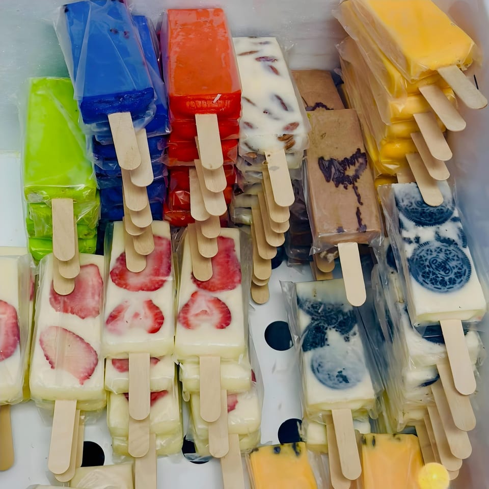 Assorted paletas, including strawberry, Oreo, mango, and other fruit flavors, in a cooler.
