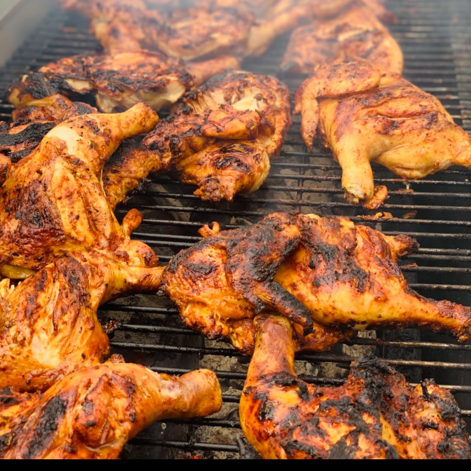Mexican grilled chicken, charred and seasoned, cooking on a smoky barbecue grill.