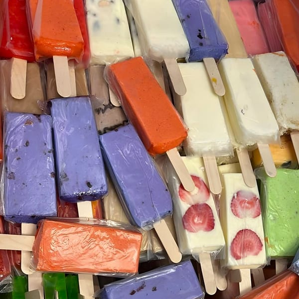 Assortment of colorful paletas, including strawberry, orange, purple, and green flavors, wrapped in plastic.