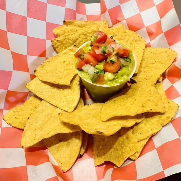 A basket of El Pollito Pio's tortilla chips with a cup of guacamole and pico de gallo.