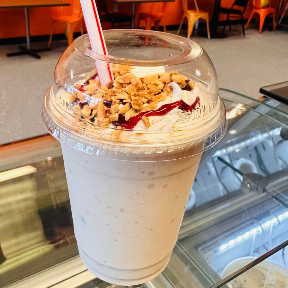 A large El Pollito Pio milkshake with whipped cream, nuts, and strawberry drizzle, with a red and white straw.