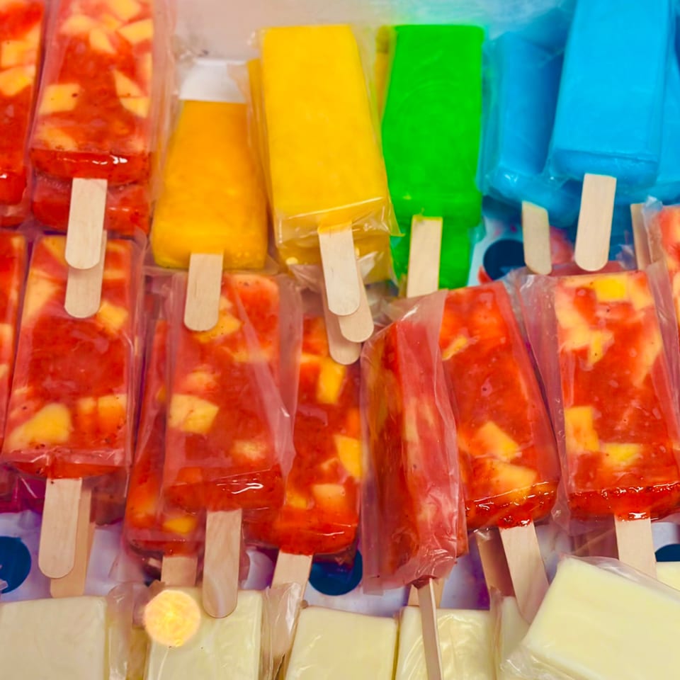 Colorful paletas, some red with fruit chunks, and others solid yellow, green, and blue.