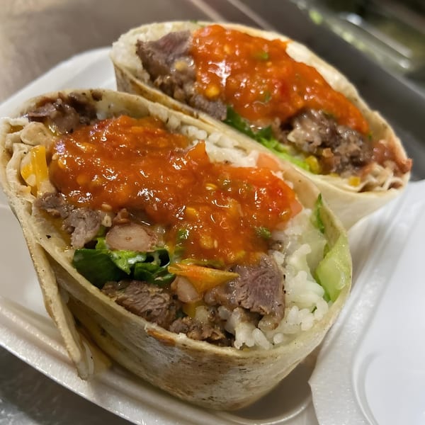 Two El Pollito Pio burritos, filled with meat, rice, lettuce, and topped with red salsa.