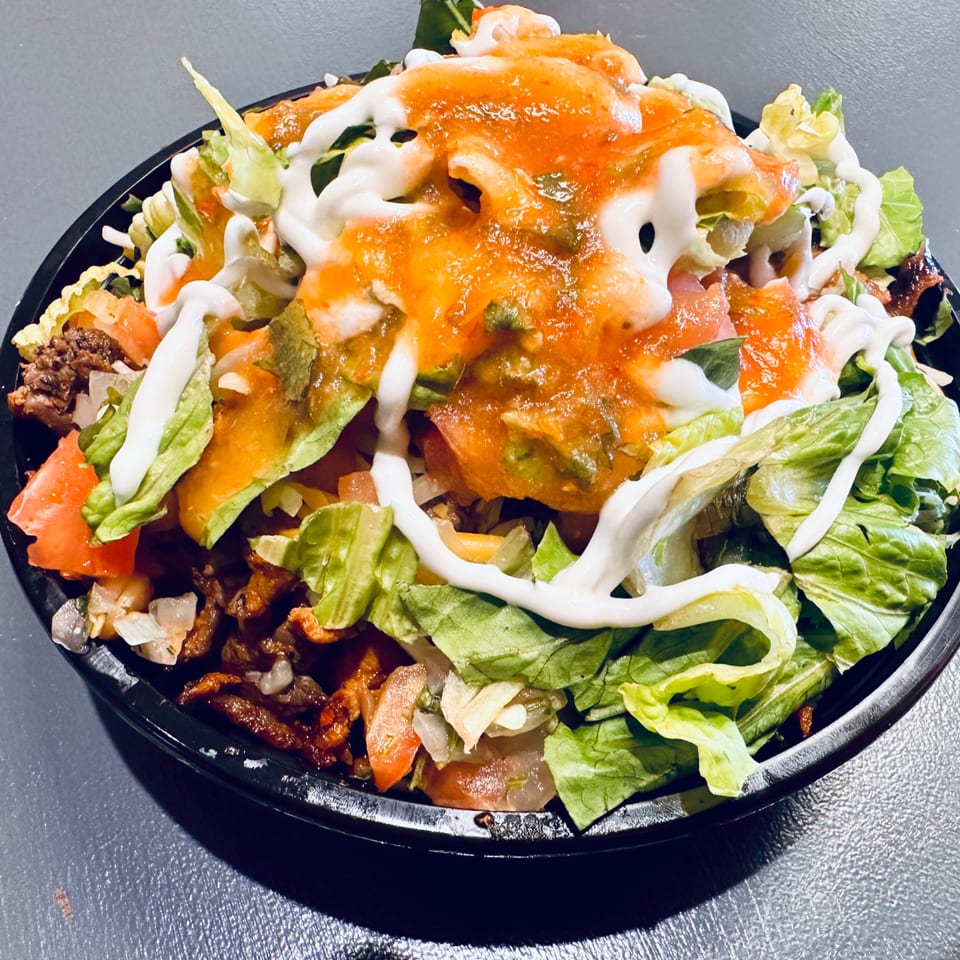 A vibrant Mexican taco salad with lettuce, tomatoes, meat, salsa, and sour cream in a black bowl.