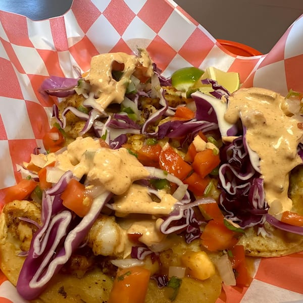 Two El Pollito Pio shrimp tacos with red cabbage, pico de gallo, and creamy sauce.